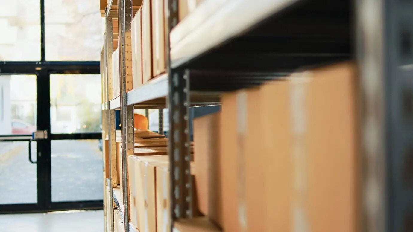 Cajas de cartón y paquetes con mercancía en un depósito, colocados en estanterías y estantes antes del envío o la distribución. Espacio de almacén vacío con paquetes de cartón y suministros de carga. Toma con cámara en mano.